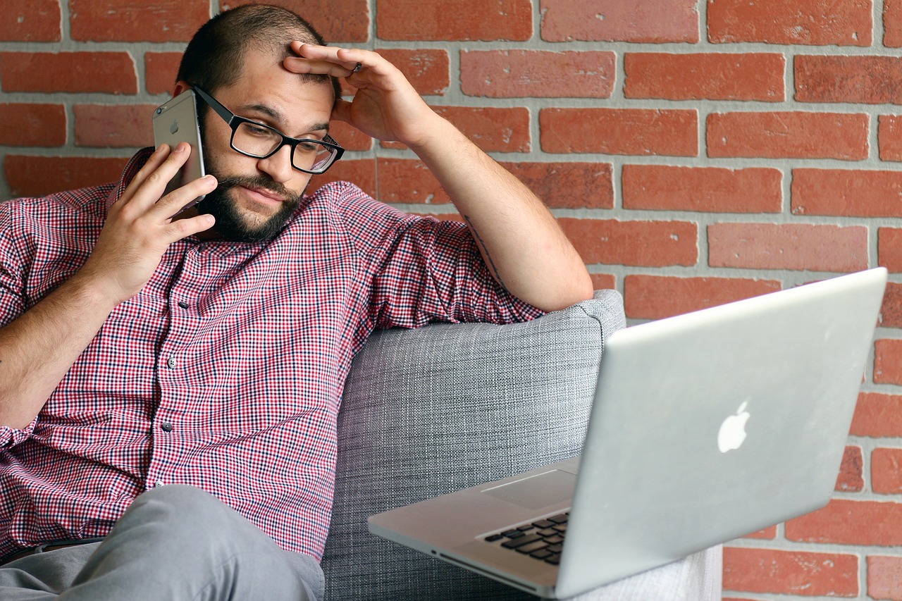 Frustrated investor looking at laptop and mobile phone with declining stock charts in the background